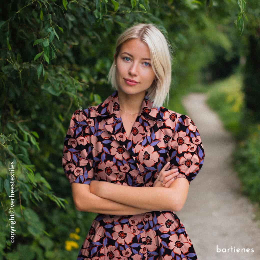 dame-mit-kleid-aus-baumwollsatin-in-navyblau-mit-großen-blumen-in-koralle-in-der-natur-vor-Waldweg