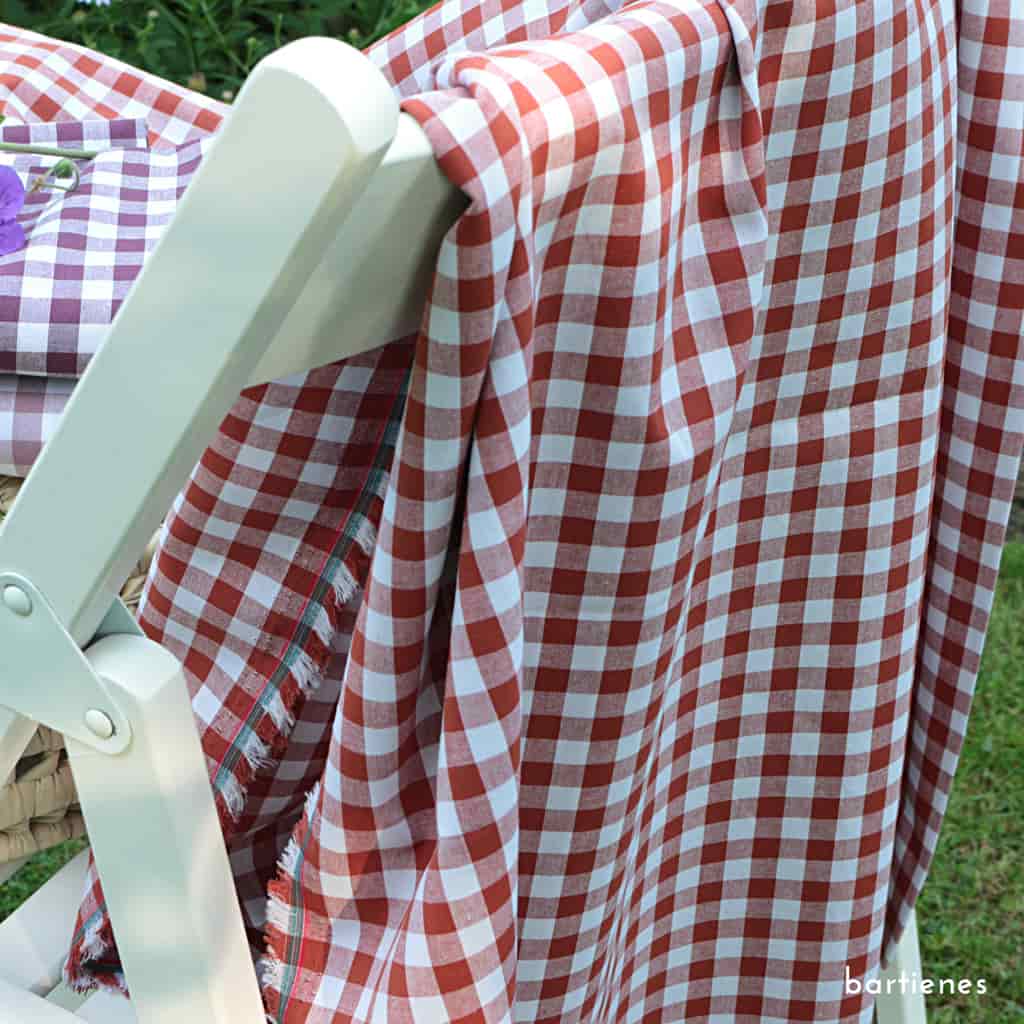 nahaufnahme-drei-karo-stoffe-gestapelt-auf-picknickkorb-im-sommergarten-vor-blumenbeet