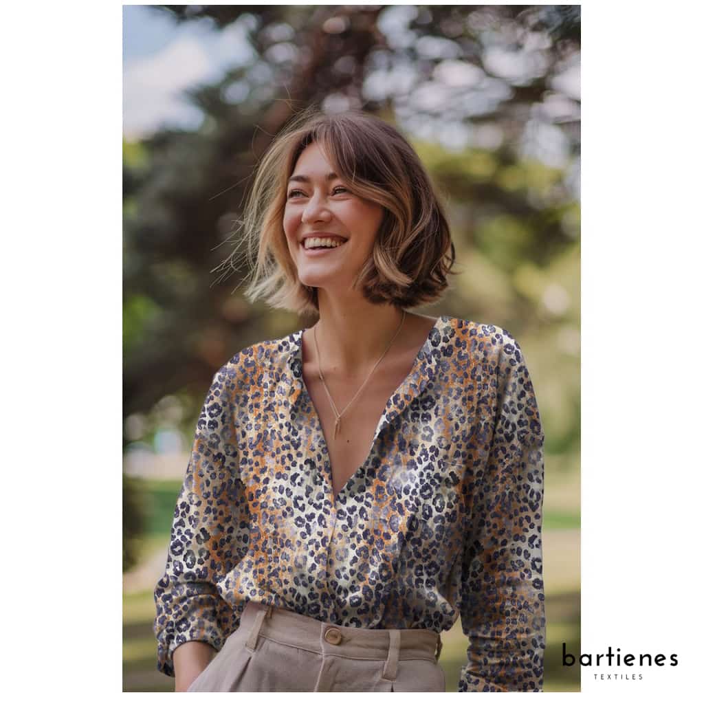 dame-mit-bluse-aus-musselin-stoff-leo-muster-auf-sand-hellbraun-und-hose-in-beige-steht-im-gruenen-und-lacht