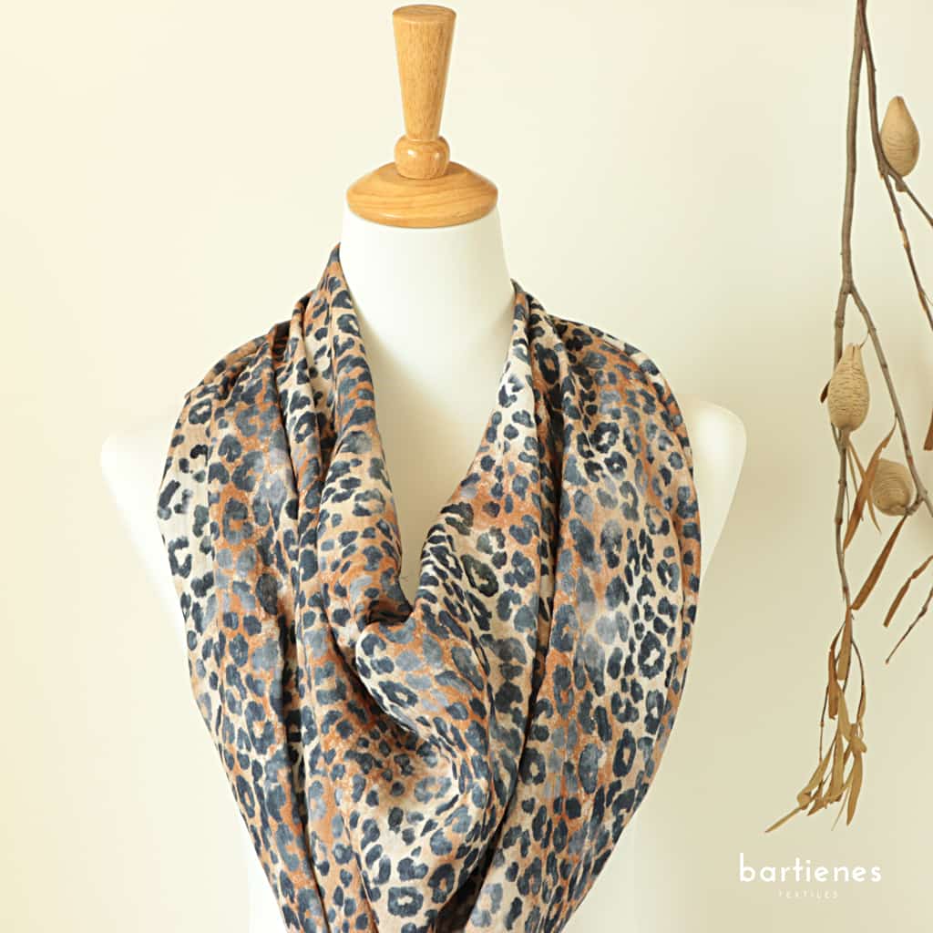 musselinstoff-meterware-mit-leo-muster-auf-sand-hellbraunem-grund-an-puppe-zum-musselintuch-drapiert-und zweig-im-hintergrund