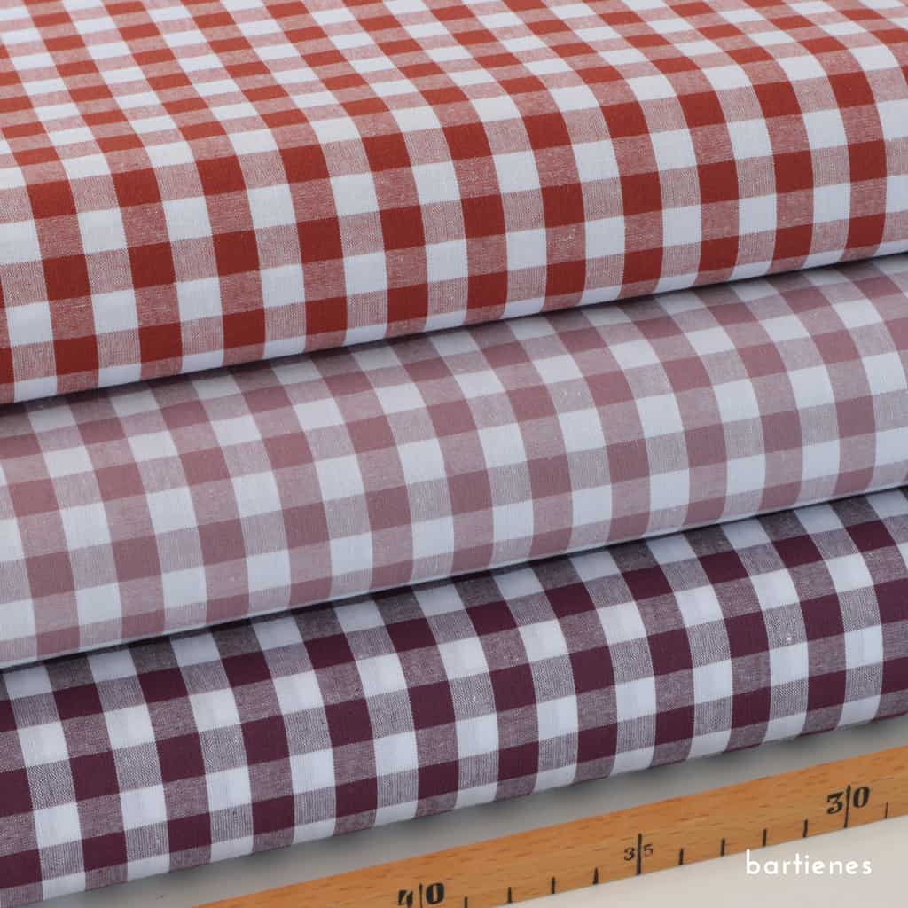 detail-von-drei-stoffballen-gestapelt-mit-baumwoll-karo-in-rost-mauve-aubergine-mit-weiss-sowie-massstock