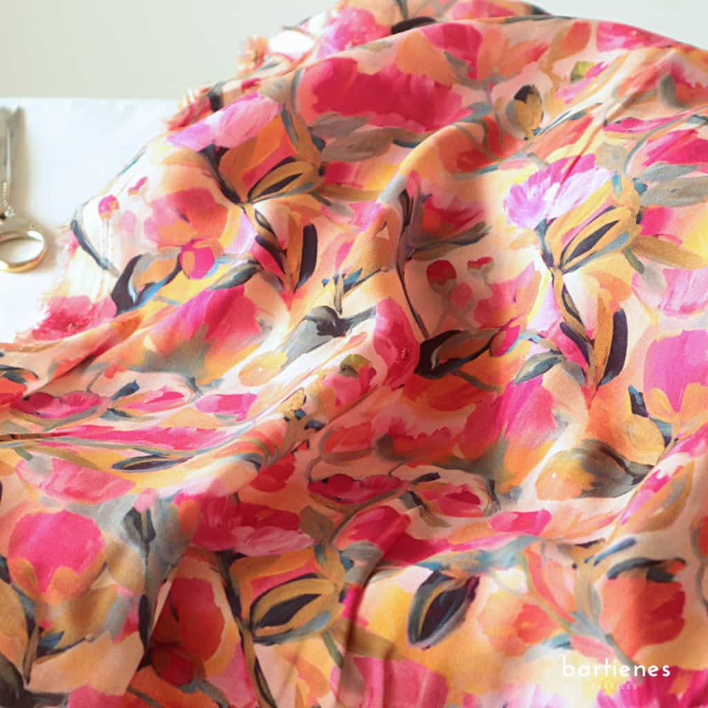 foto-nahaufnahme-von-stoffballen-viskose-stoff-in-flieder-mit-grossen-stilisierten-blumen-in-lila-und-orange